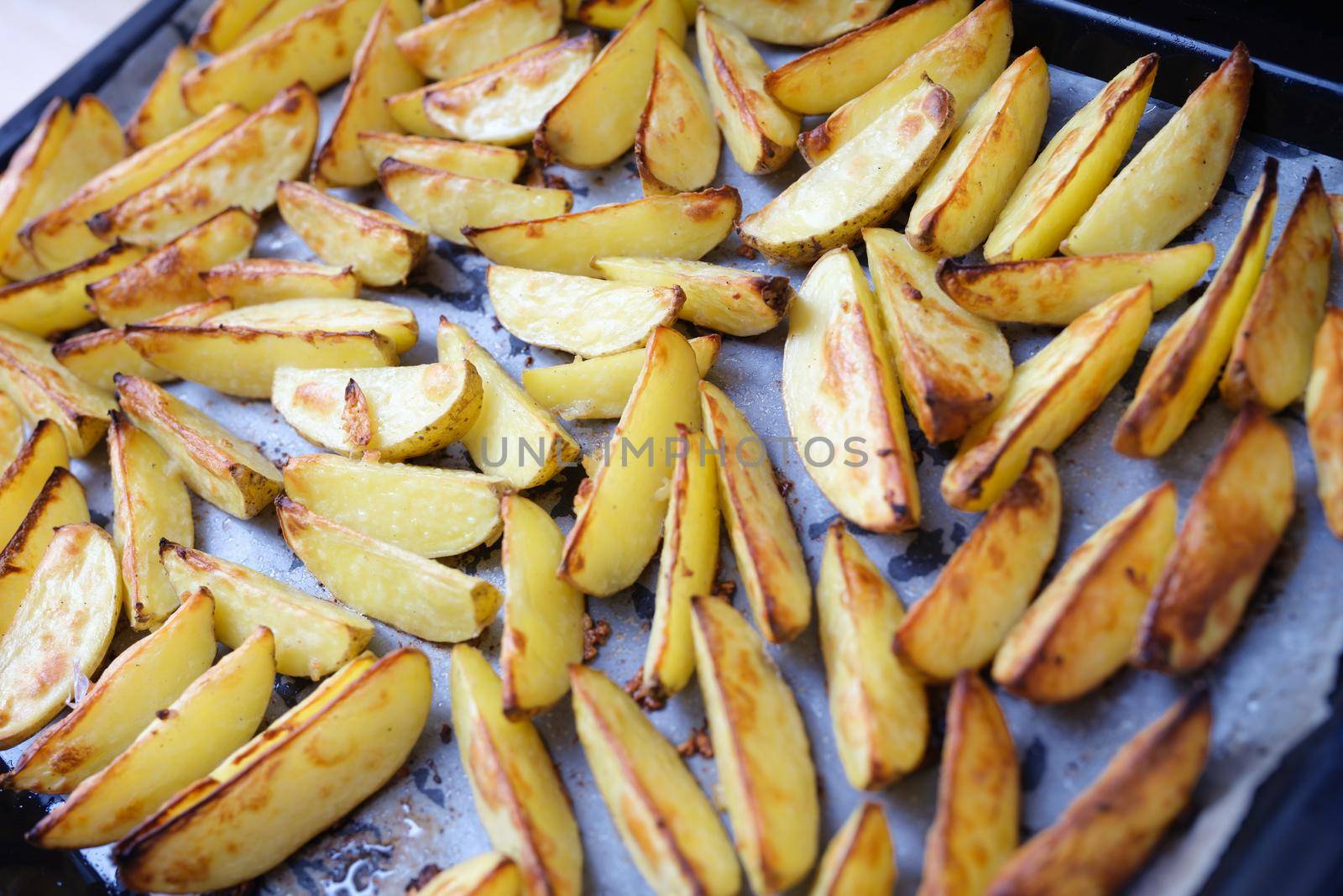 Baked potato wedges on a parchment baking sheet, close-up. Crispy vegetables for lunch, fresh homemade food