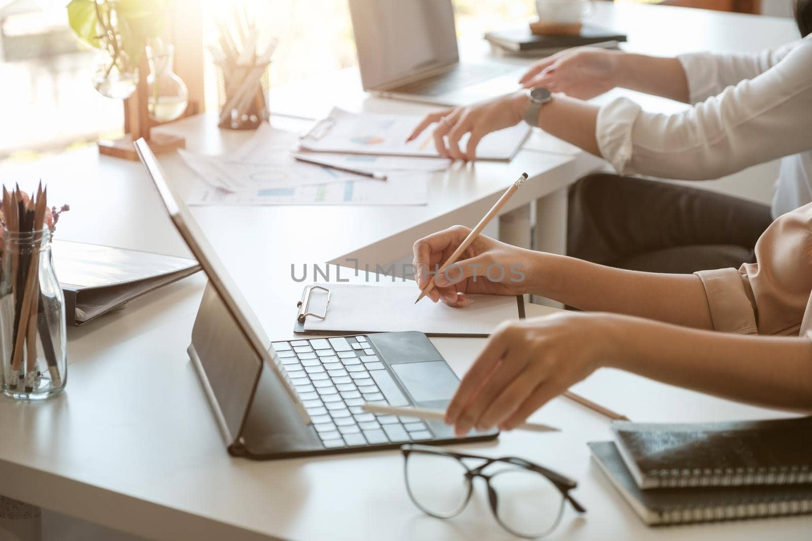 Business women hand are taking notes on paper with a black pen, and she is using a laptop computer on a woeking desk in the office.