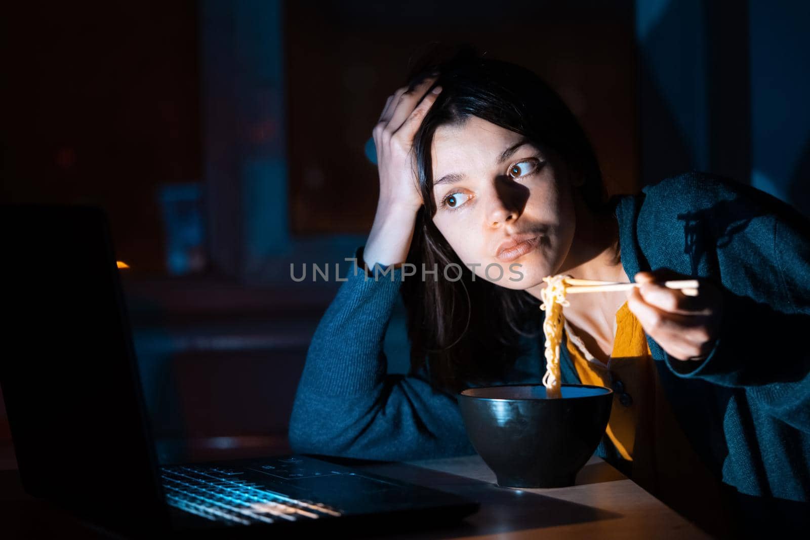 Girl eats noodles and works on a laptop. by africapink