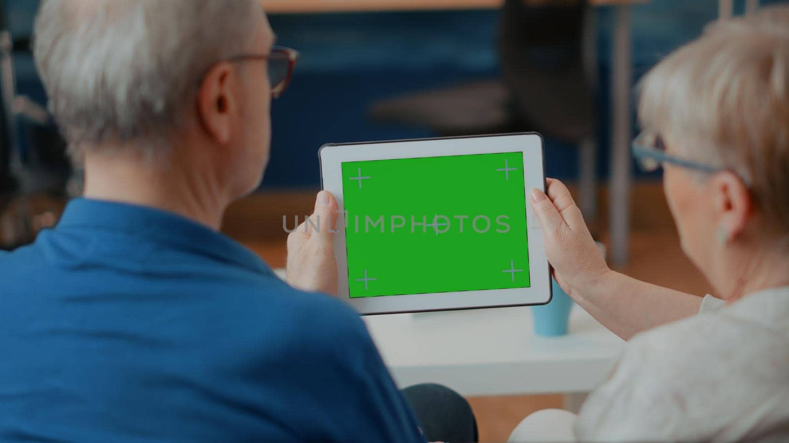 Old couple looking at green screen template on digital device, analyzing blank copy space and isolated chroma key with mock up background. Retired people using modern technology on display.