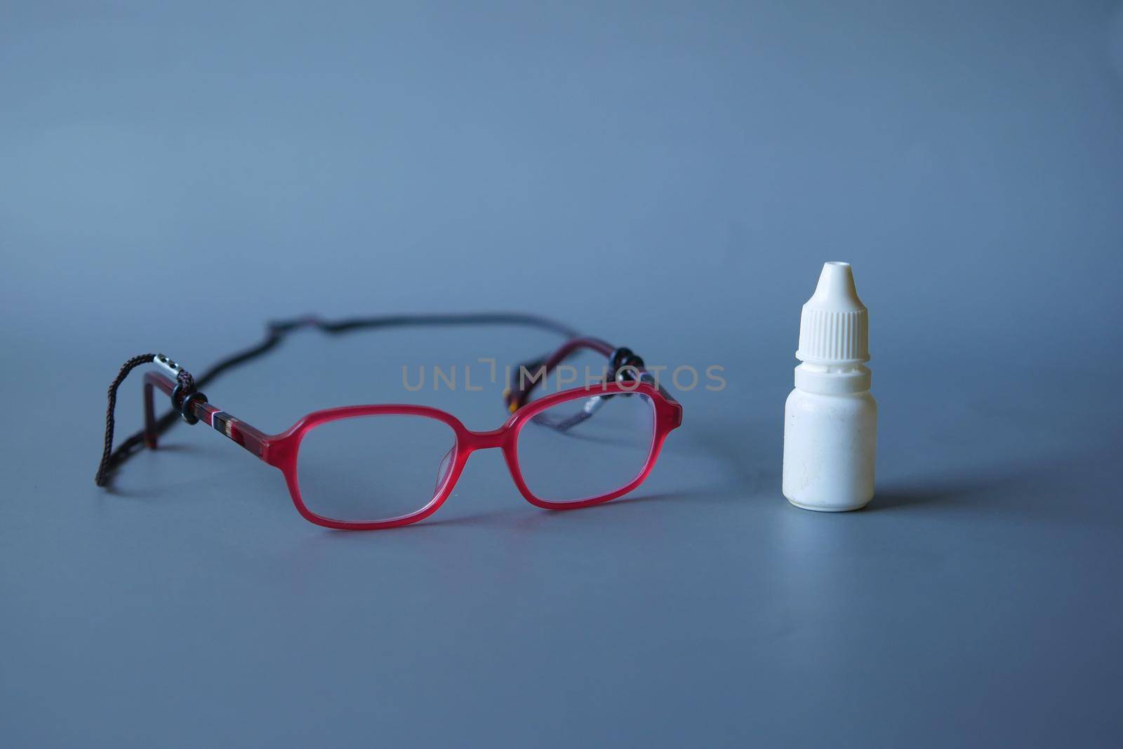 close up of eye drop bottle and eyeglass on black .