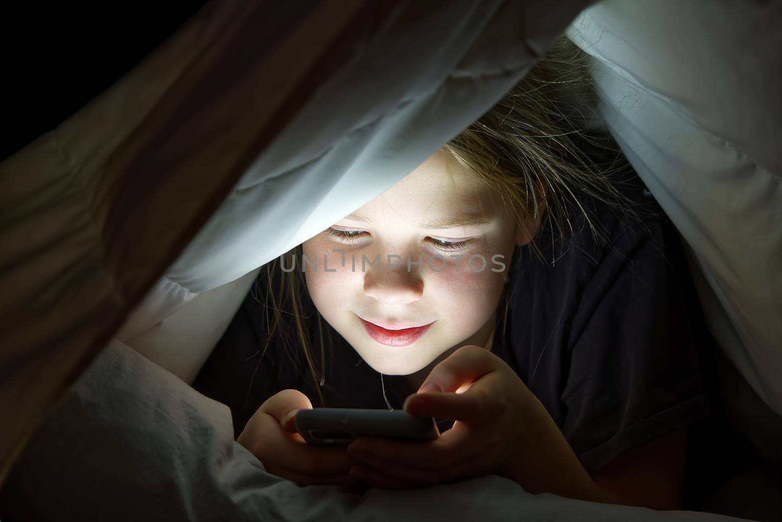 Portrait of girl with mobile phone under blanket at night. Gadget night. Social media addiction. Online communication. by PhotoTime