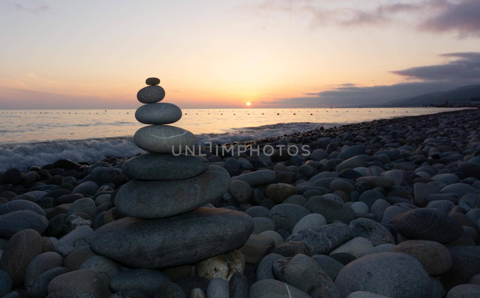Stack of gray zen stones on the beach at sunset, beautiful seascape. Made of stone tower as rest balance vacation concept.