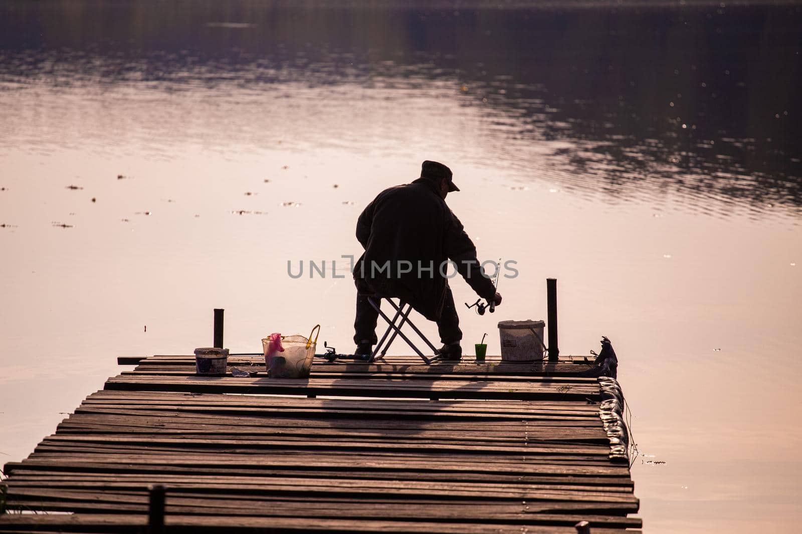 silhouette of a fisherman from behind sitting on a wooden pier during evening fishing.