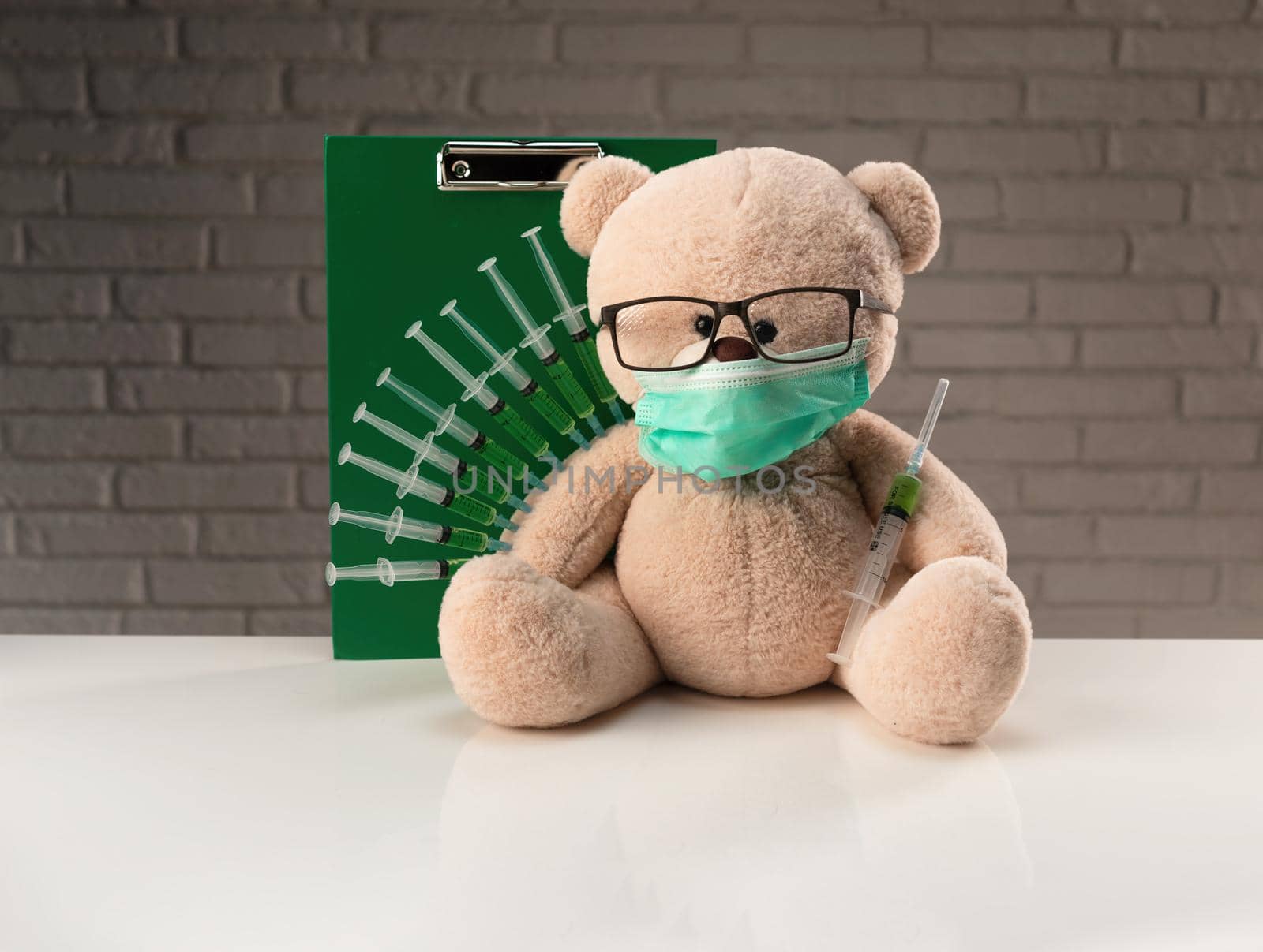 teddy bear in a medical mask with syringes in his shoulder on a white medical table