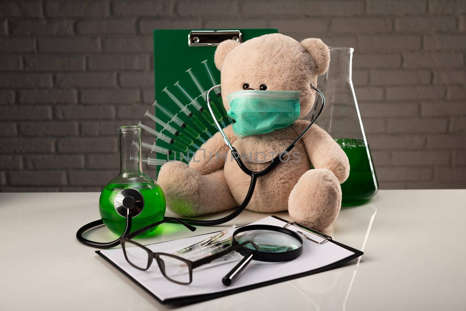 teddy bear in a medical mask with syringes in his shoulder on a white medical table with medical instruments