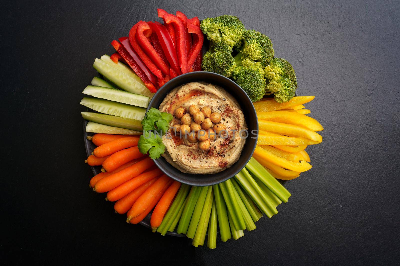 Top view of tasty chickpeas hummus in black plate with fresh vegetables on a black background. High quality photo