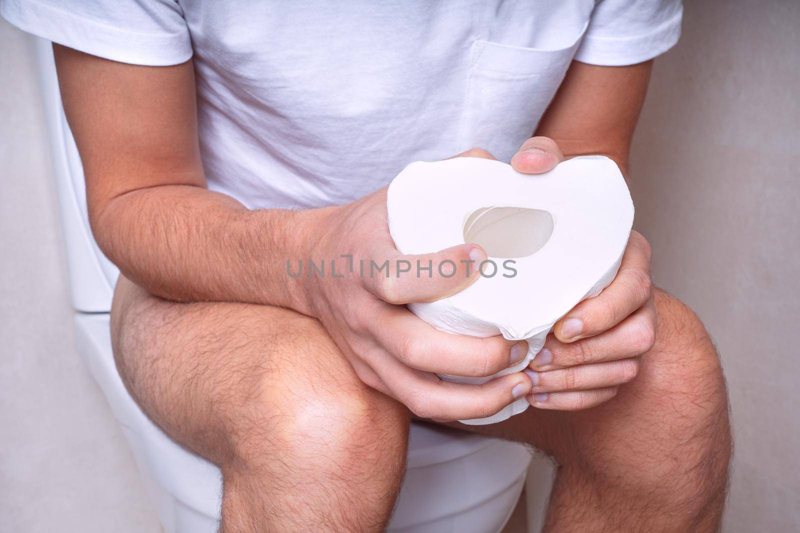 Man sitting on the toilet with toilet paper and suffering from constipation, diarrhea, stomach ache or cramps. High quality photo