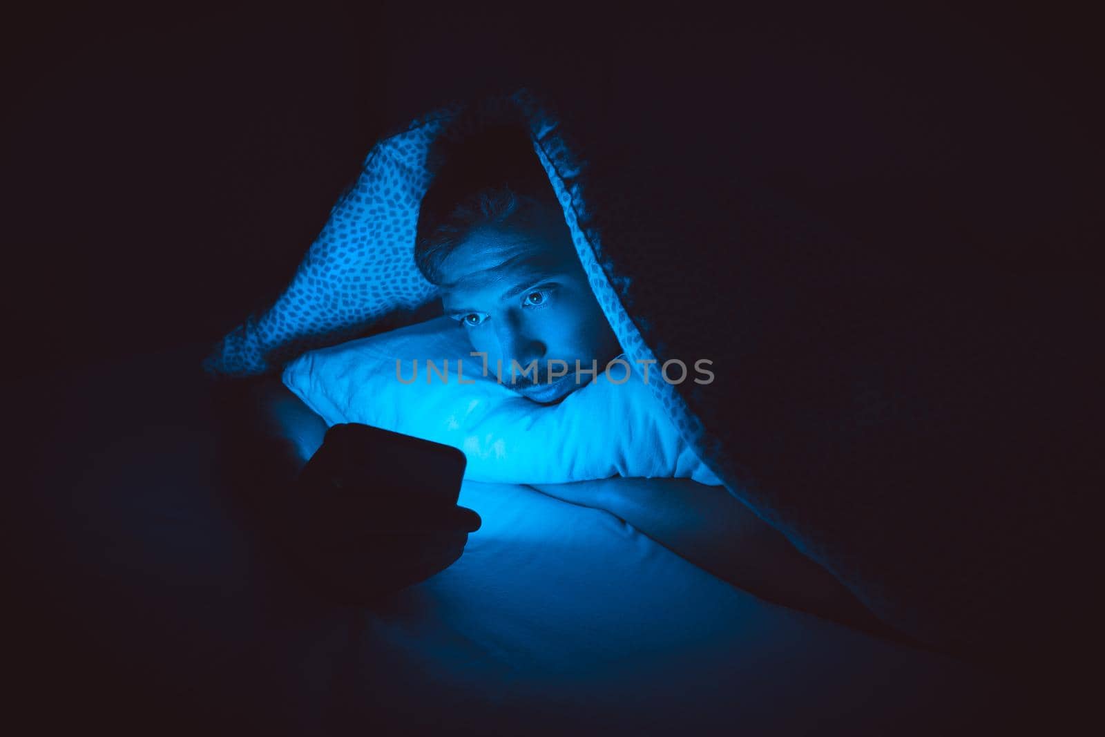 Young man lying in bed and using smartphone before sleep. Social media addiction and insomnia. High quality photo