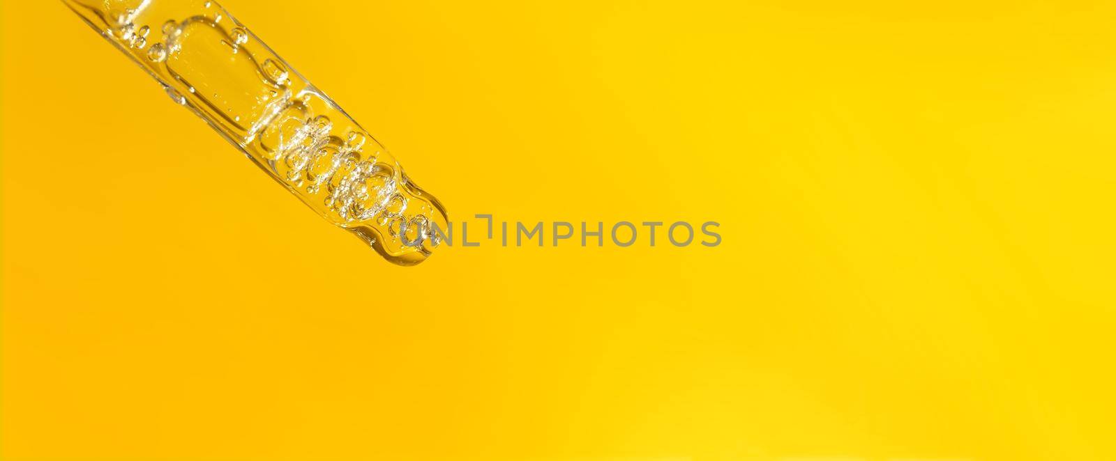 Banner of pipette with hyaluronic acid on yellow background. Cosmetics and healthcare concept closeup. Dose of serum or retinol with air bubbles. Flat lay. Luxury beauty product presentation in macro