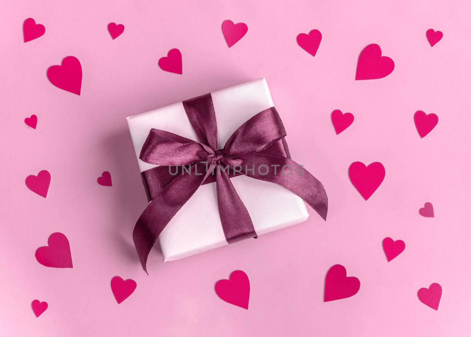 Gift in white wrapping paper on pink background with red purple hearts. St. Valentines Day, love, tenderness, friendship, and care concept. Cozy, festive, romantic wallpaper