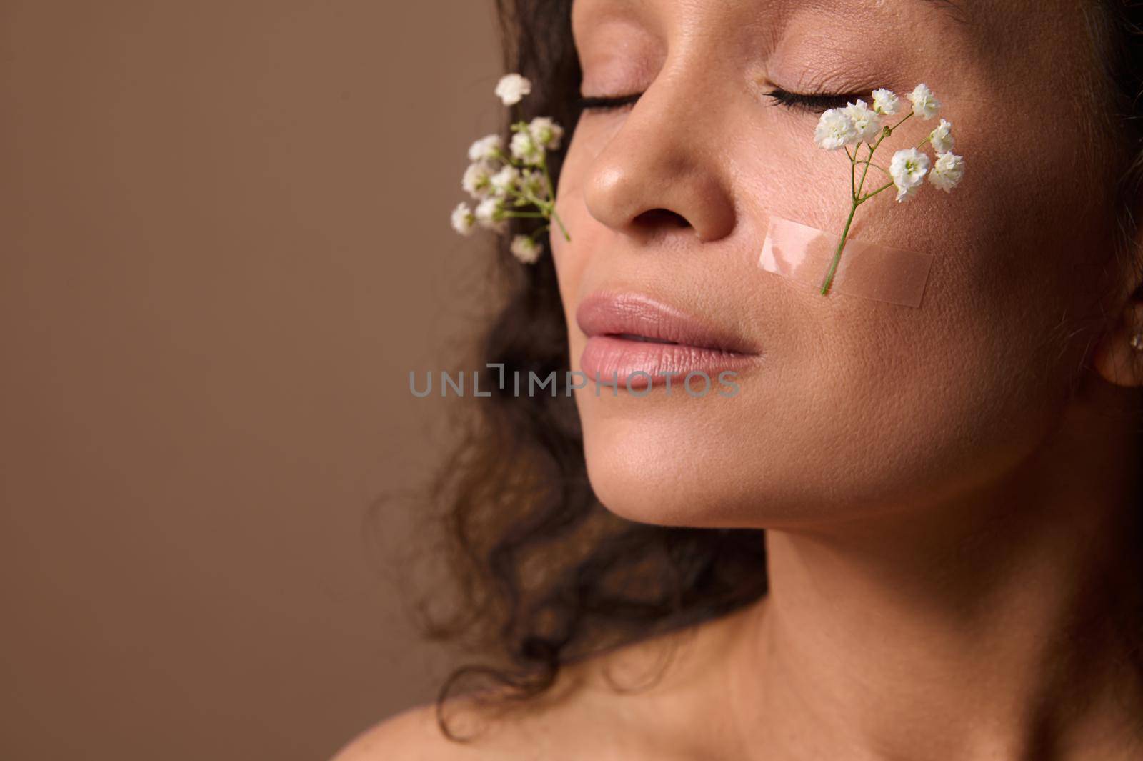 Close-up beautiful woman's face with Gypsophila white sprig on cheeks. Spring, femininity, sensuality, natural beauty people and Women's Day concept on beige background with copy ad space