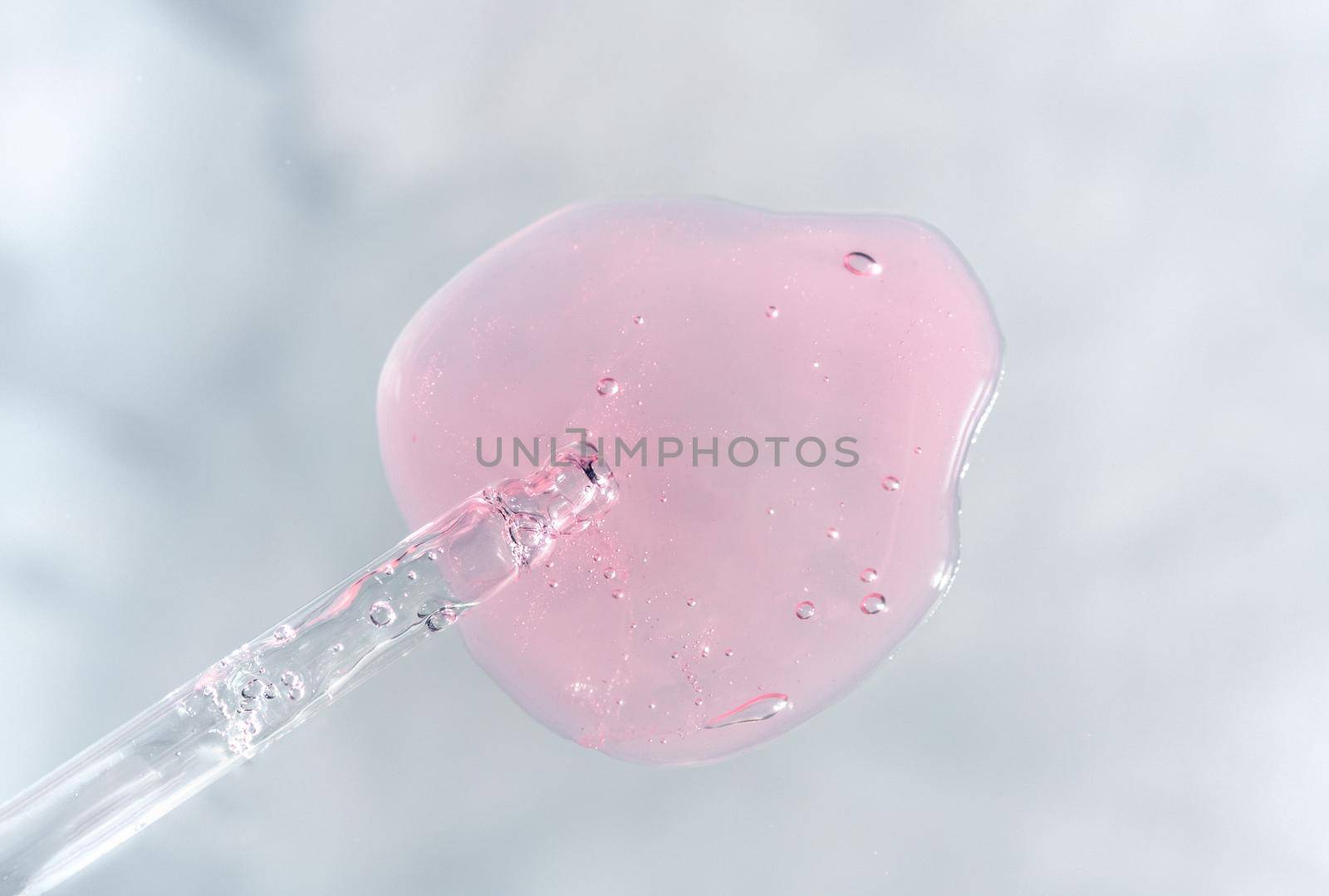 Pipette with pink fluid hyaluronic acid on gray background. Cosmetics and healthcare concept. Dose of serum or retinol with air bubbles. Flatlay. Luxury gel or beauty product presentation in macro