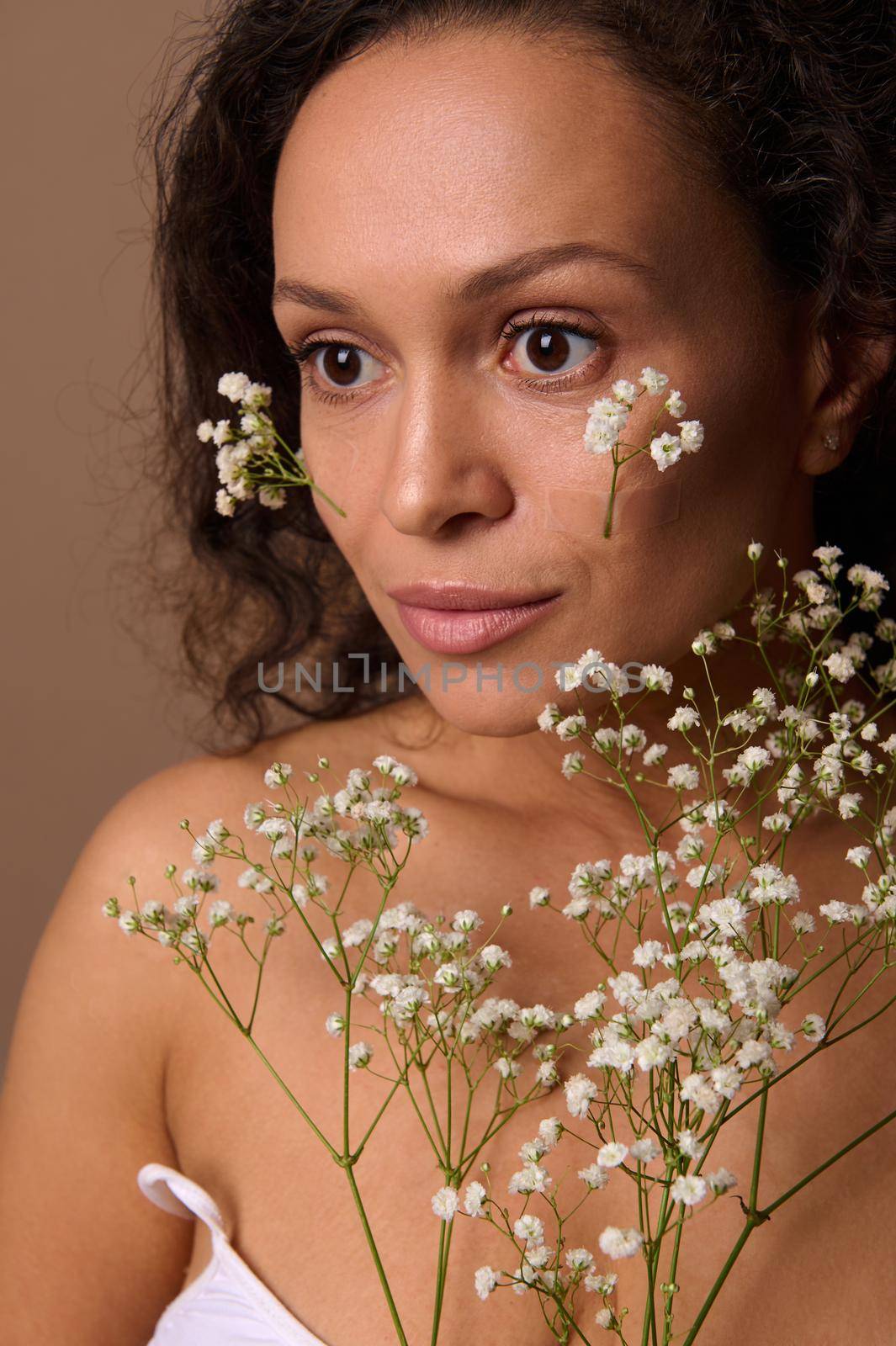 Beauty portrait of a beautiful confident serene dark-haired Hispanic woman with white gypsophila sprig. Body care, positivity, sensuality, confidence, self-acceptance, femininity, Women's day concept by artgf