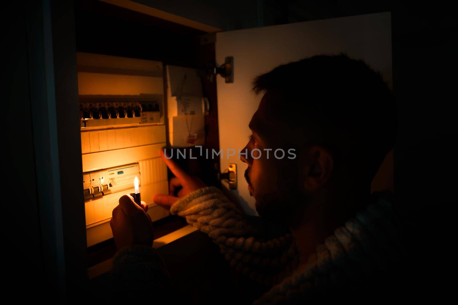 Man in total darkness investigating fuse box at home during power outage or blackout. No electricity