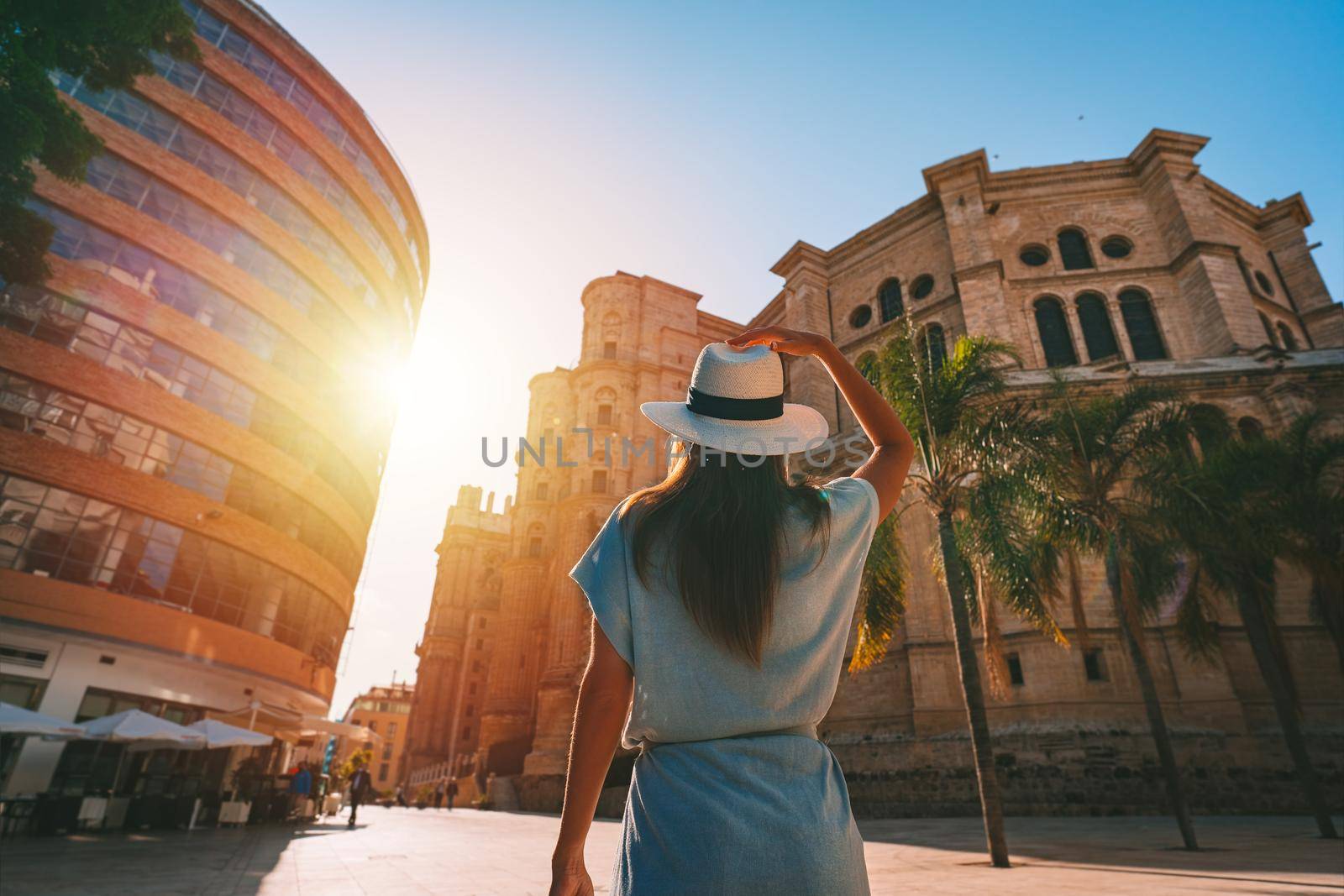 Rear view of young tourist woman in white sun hat walking in Malaga city at sunset. Summer holiday vacation in Spain. High quality photo
