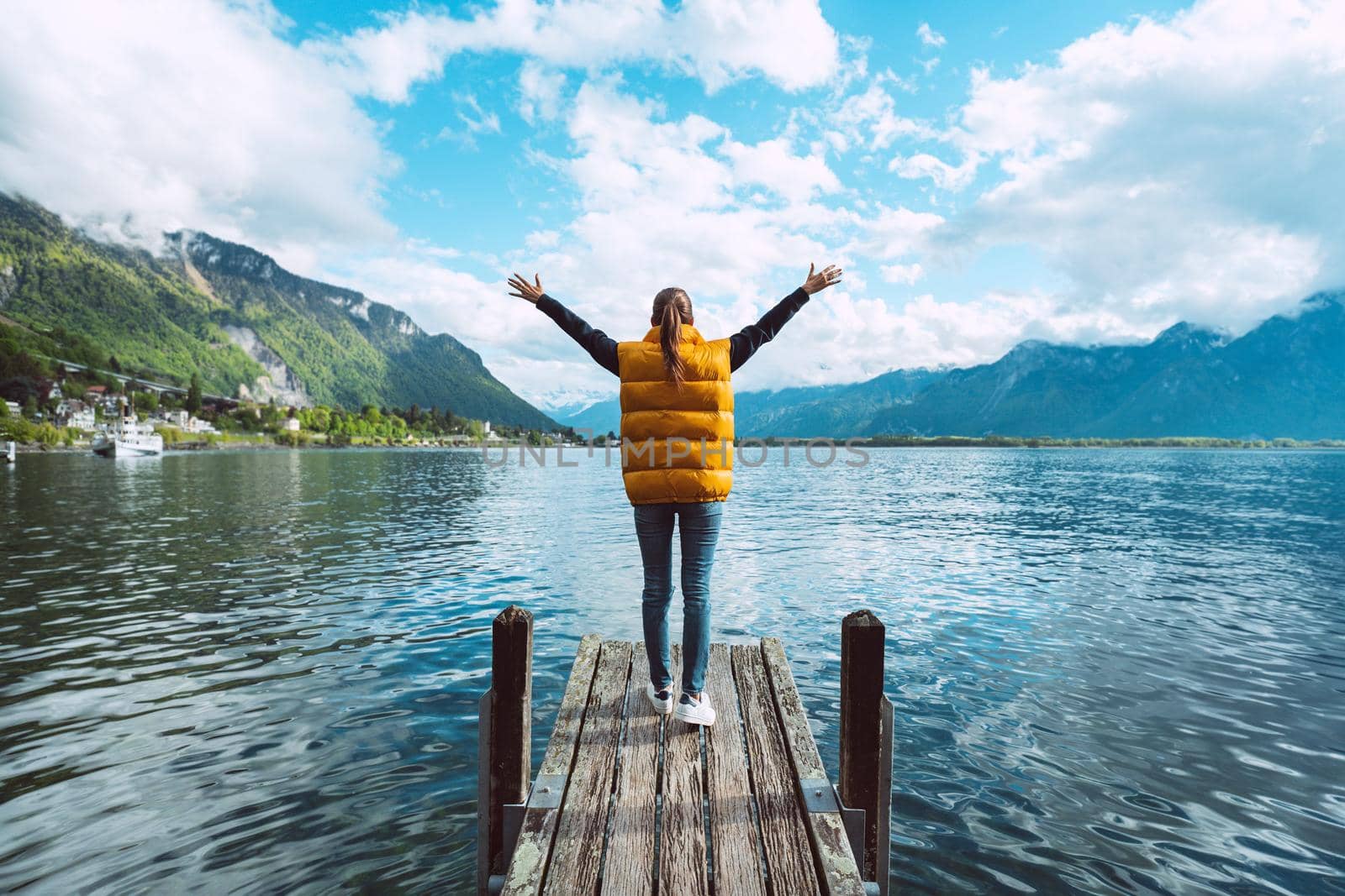 Young woman traveler with open arms standing on wooden bridge and enjoying great view on Geneva lake in Switzerland by DariaKulkova