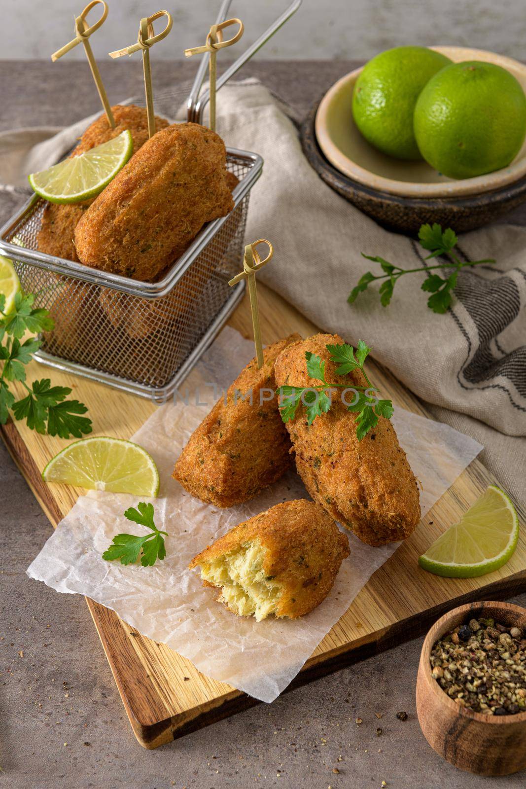 Cod dumplings, or "bolinhos de bacalhau" and parsley leaves and lemons on wooden cutting board in a kitchen counter top.