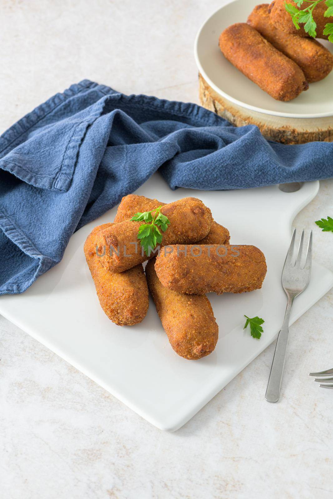 Meat croquets and parsley leaves on white ceramic dishes in a kitchen counter top.