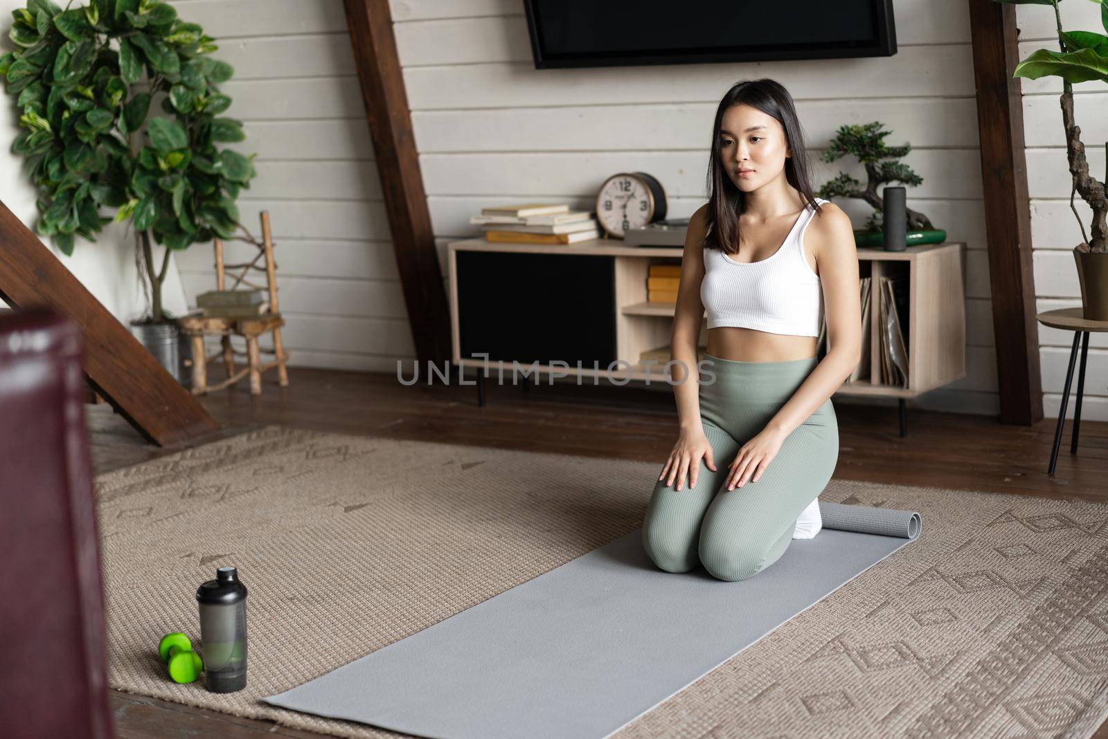 Image of young asian woman doing yoga at home on floor mat, meditating in activewear in living room.