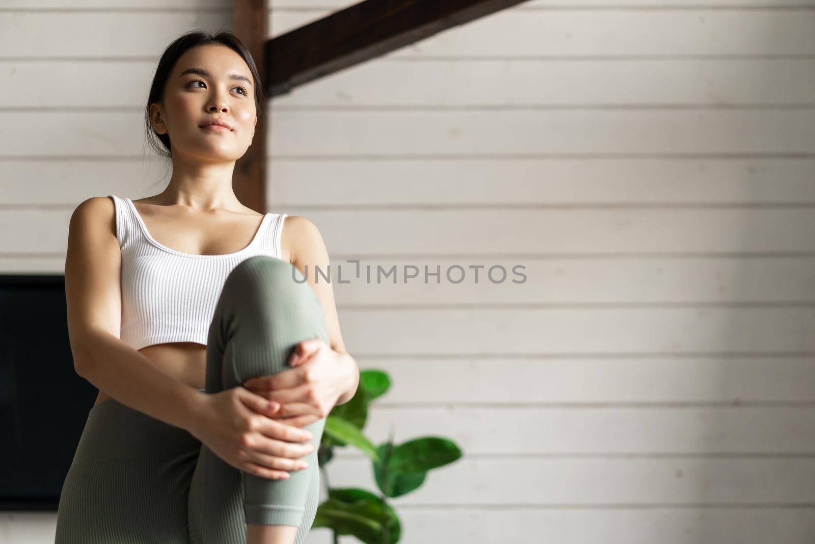 Portrait of asian girl doing workout at home, lifting legs and looking at distance, exercising in living room without fitness gear.