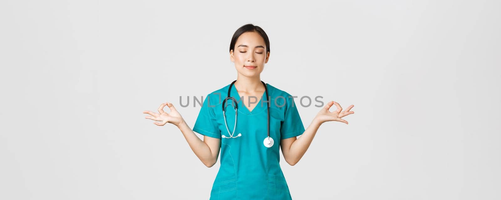 Covid-19, healthcare workers and preventing virus concept. Calm and patient asian female doctor, nurse in scrubs staying relaxed, meditating with eyes closed and happy smile, white background by Benzoix