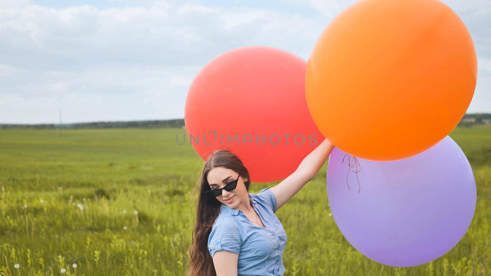 Happy girl with big multicolored balloons posing on the field. by DovidPro