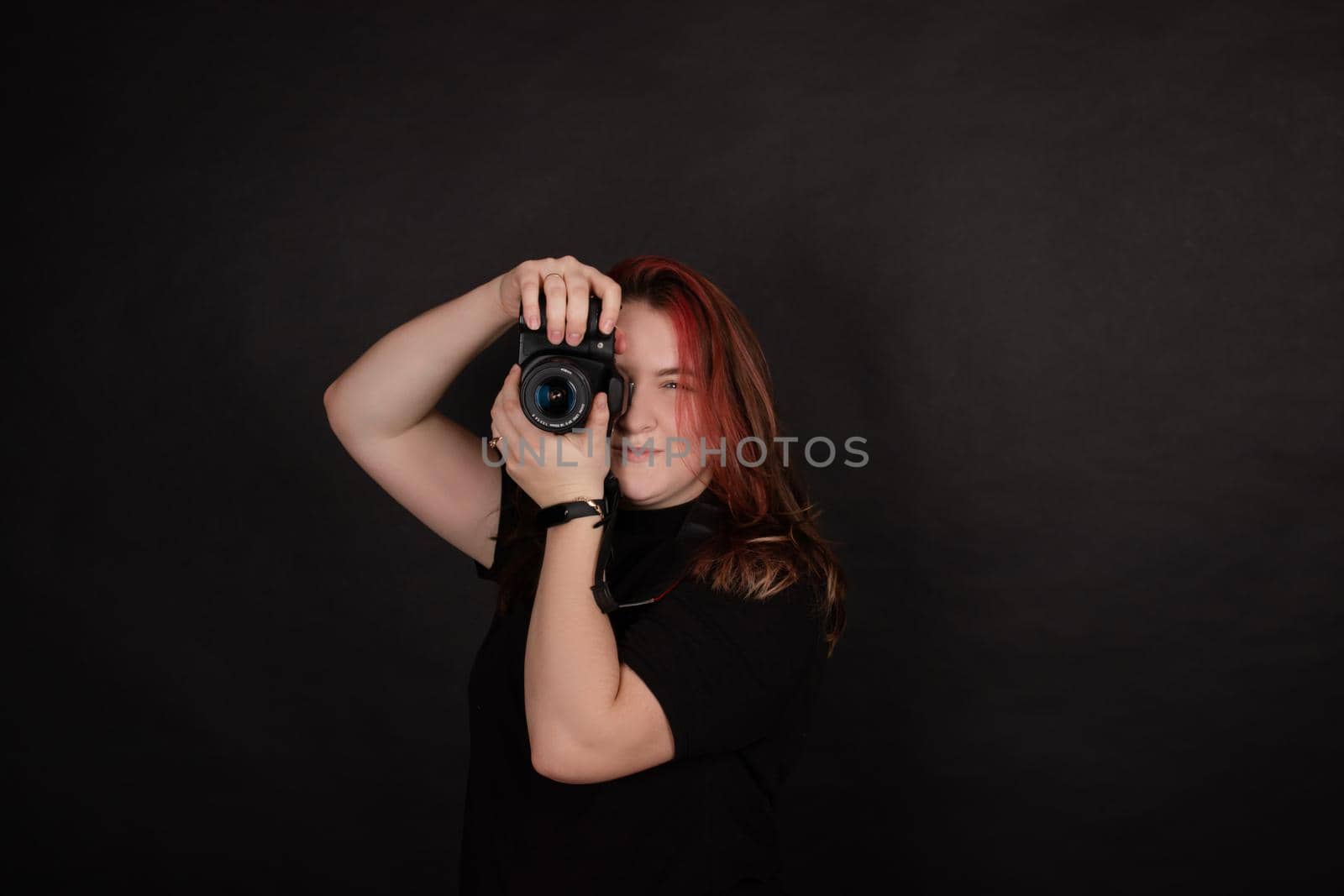 redhead girl with a professional camera posing on black background. woman female photographer