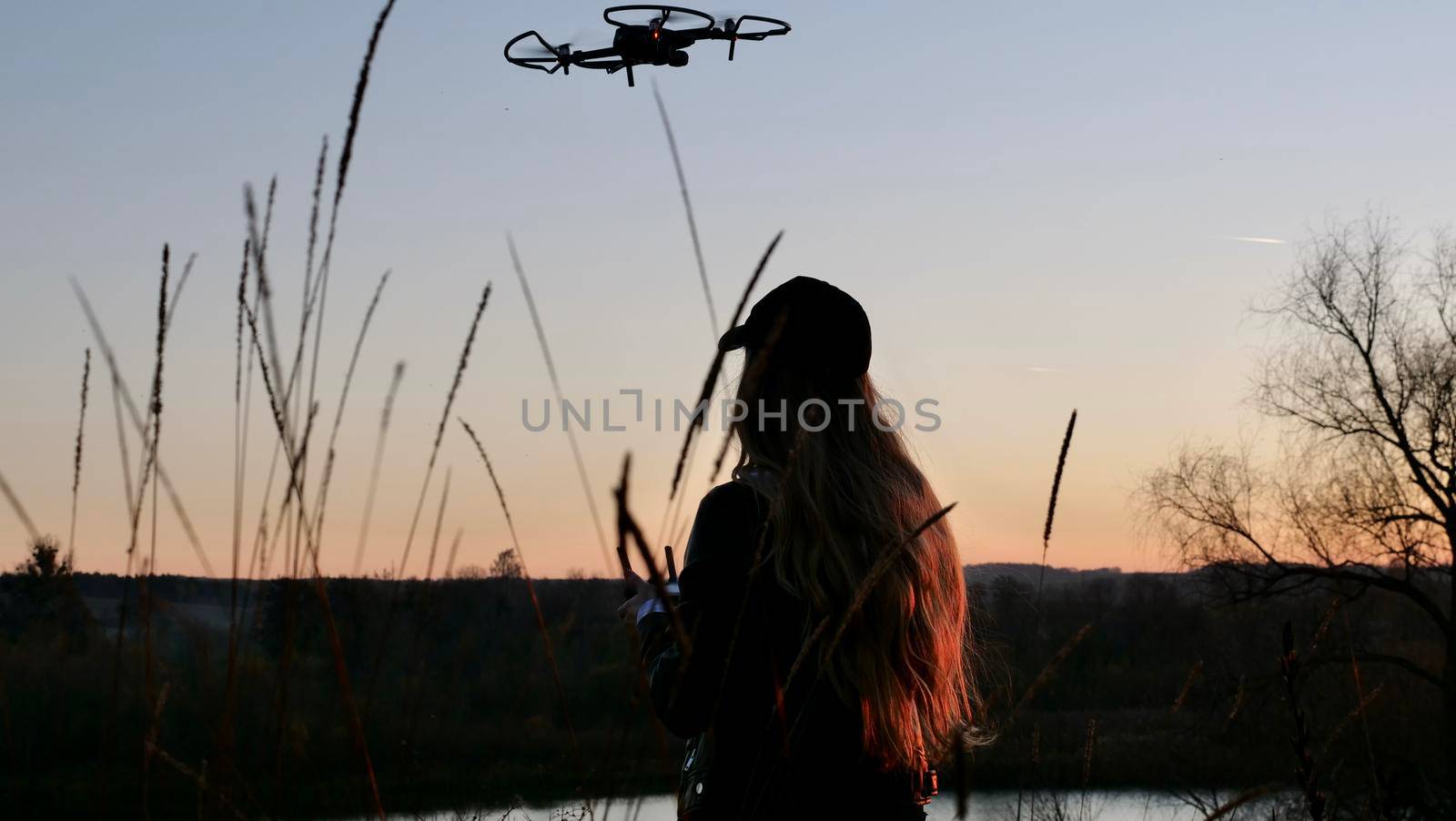 Female videographer pilots a quadcopter at sunset. Silhouette woman, girl of a pilot and a drone