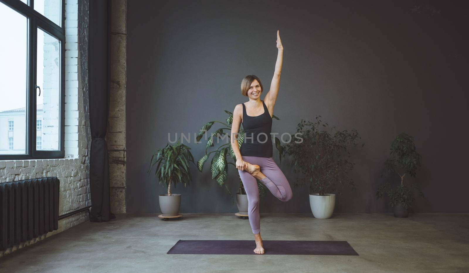 Lonely Woman in Sportswear Doing Side Plank in a Spacious Yoga Studio. Sporty Fit Woman Practices Hatha Yoga. Full Length. Gray Background. High quality photo