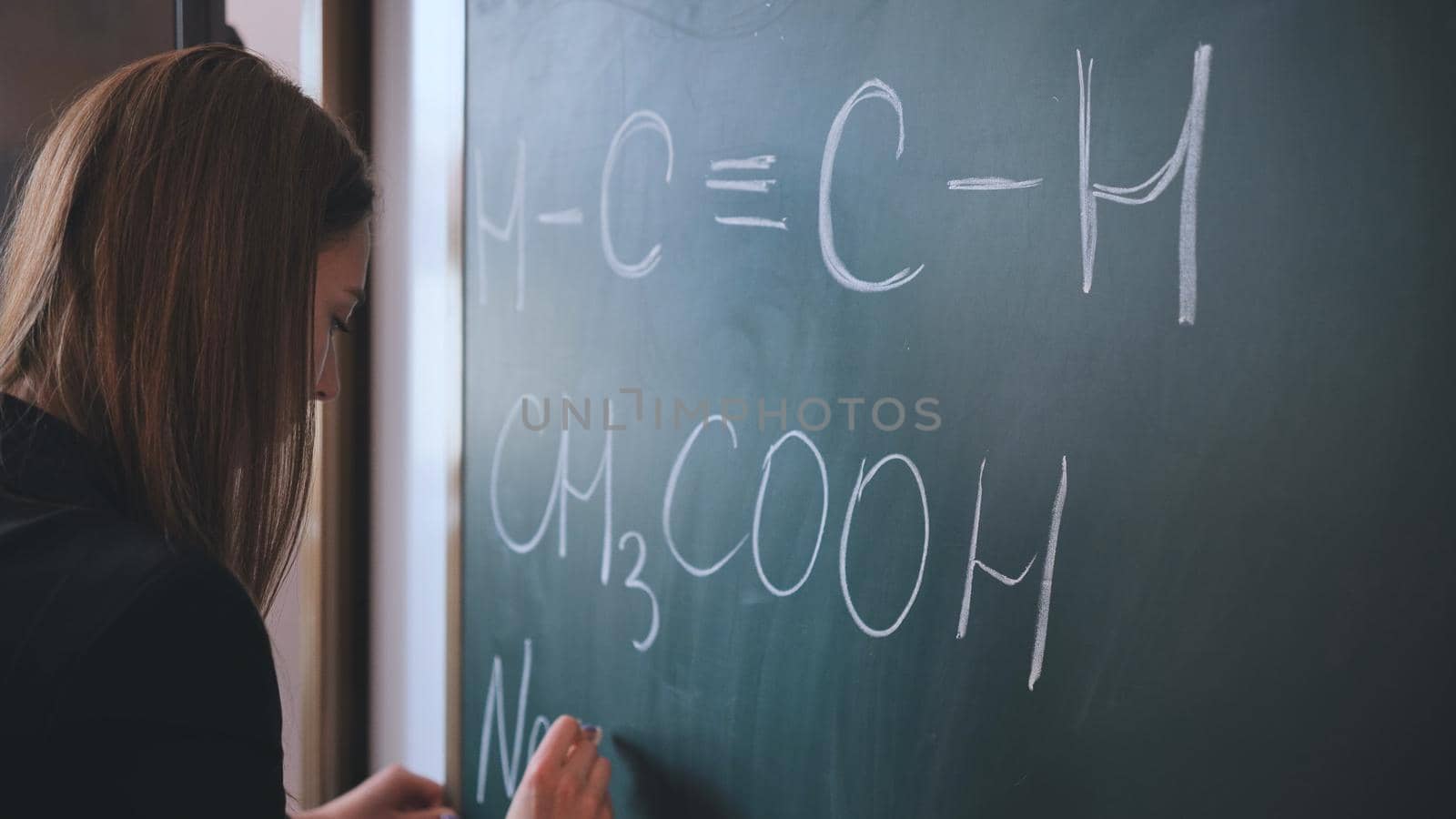 The girl is writing a chemical formula on the blackboard in the classroom