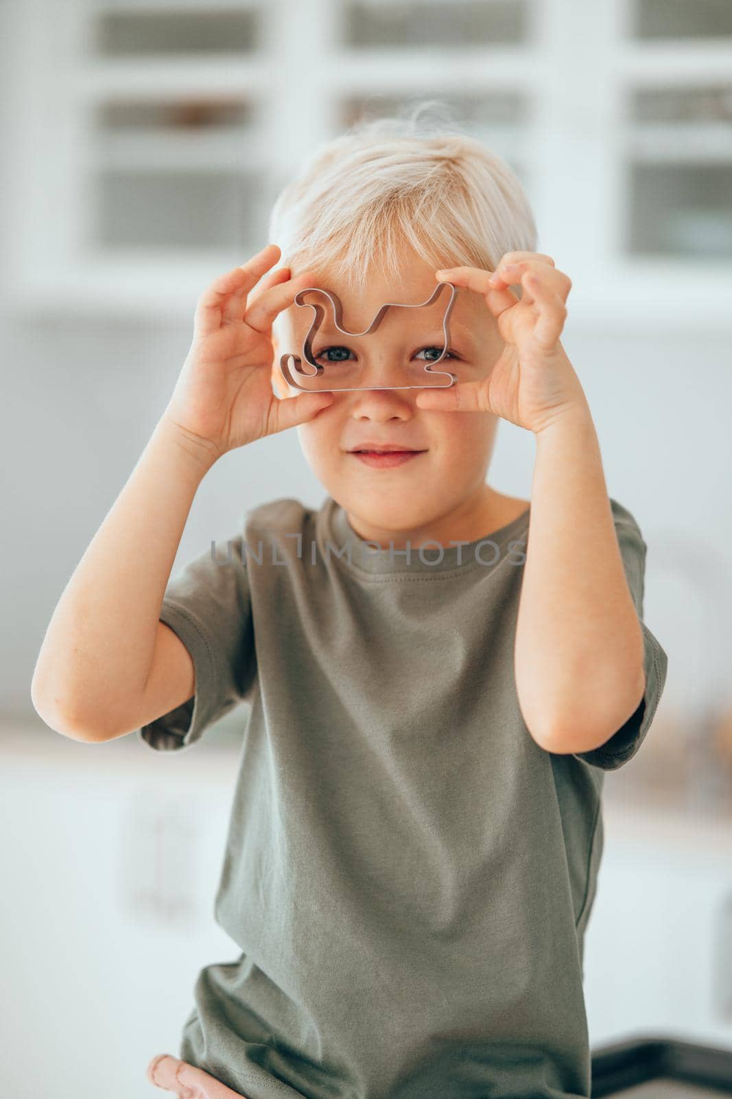 Little caucasian boy holding and looking through a Christmas cookie cutter. by XGroup