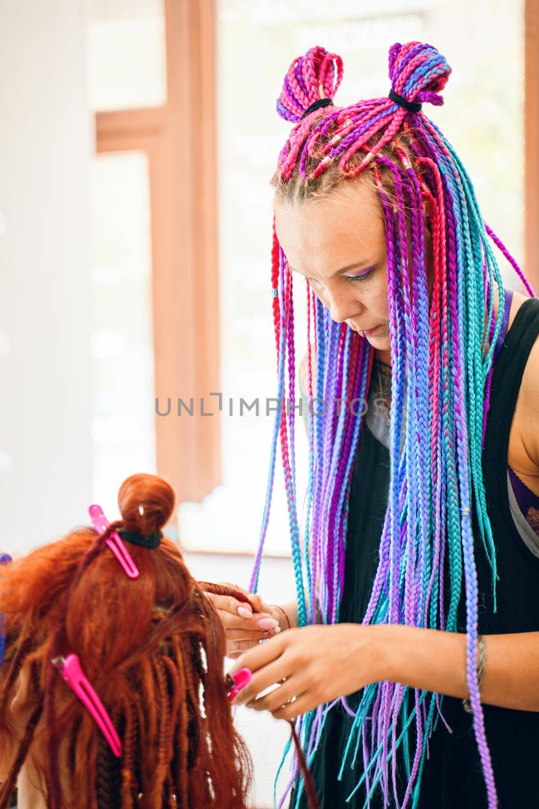 Female hairdresser weaves to funny redhead girl ginger afro pigtails. Barber braids dreadlocks. Hippie and boho style coiffure with kanekalon. Beauty salon services.