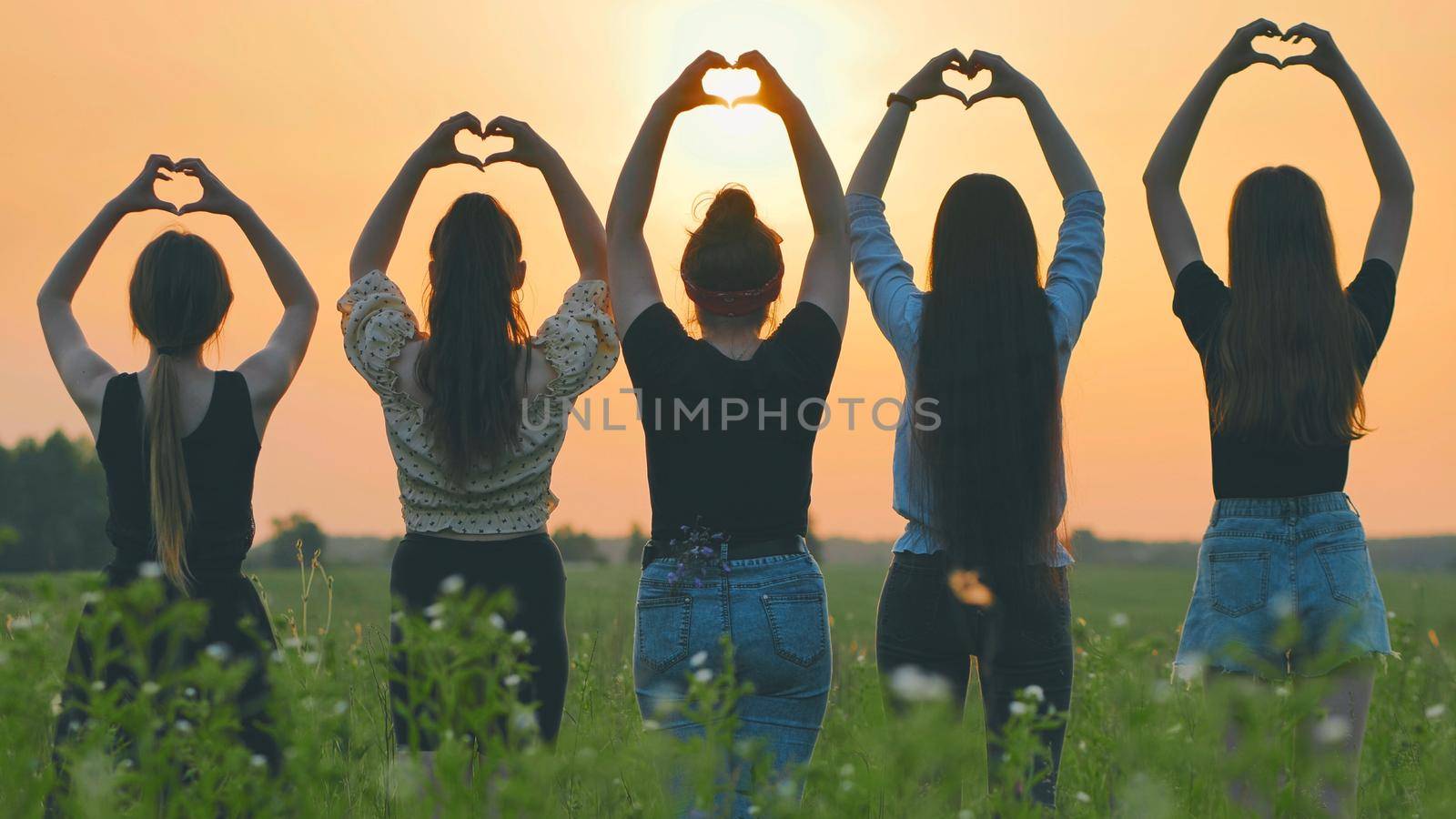 Five girls make a heart shape from their hands at sunset