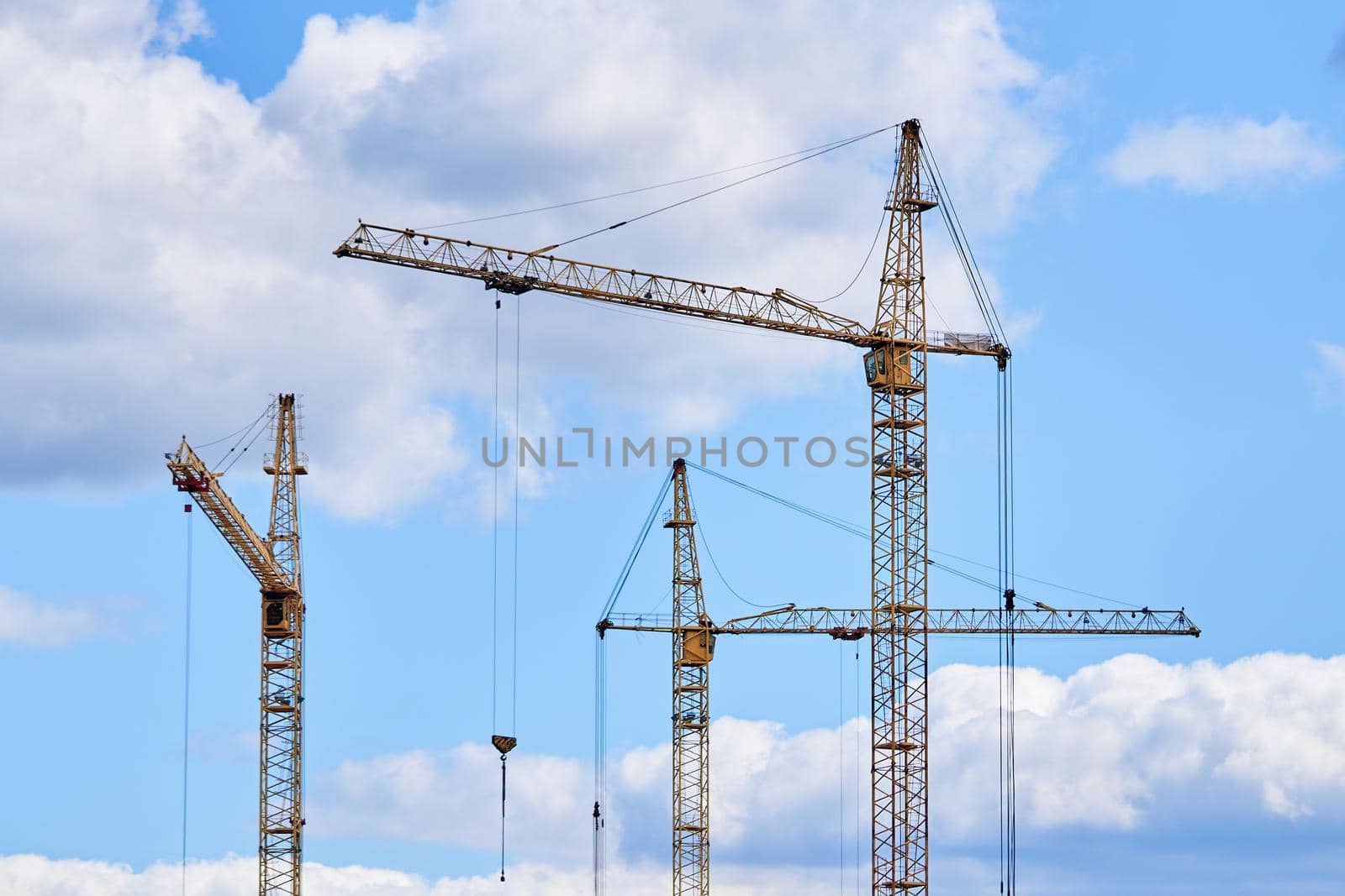 Industrial building cranes on background of cloudy sky. Hoisting cranes for creating multi-storey buildings of new city districts. Construction site background.