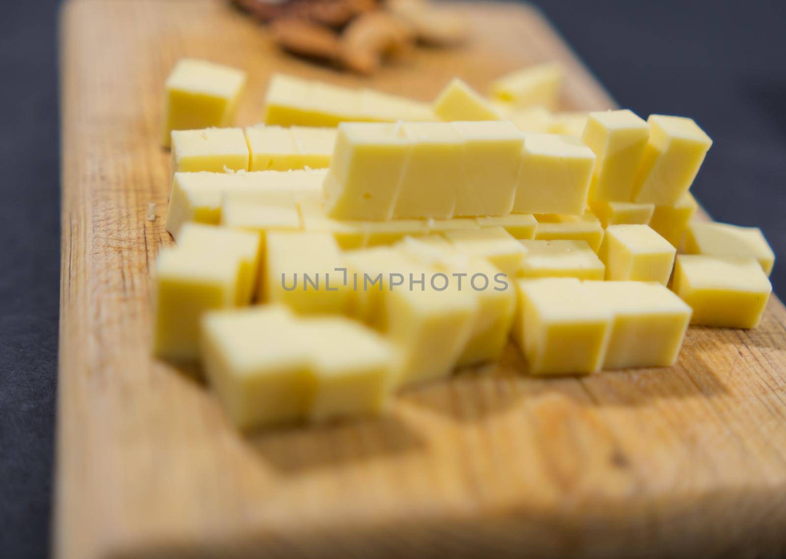 Close-up of diced yellow cheese and blurry walnuts on cutting board. Wooden board with fresh cheese cubes and nuts above black surface. Healthy snacks and balanced diet
