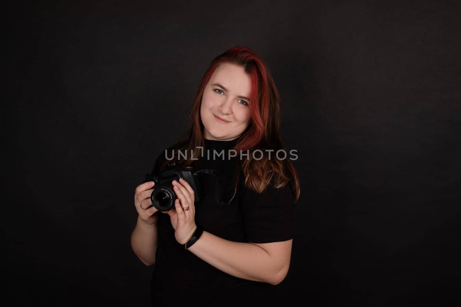 redhead girl with a professional camera posing on black background. woman female photographer