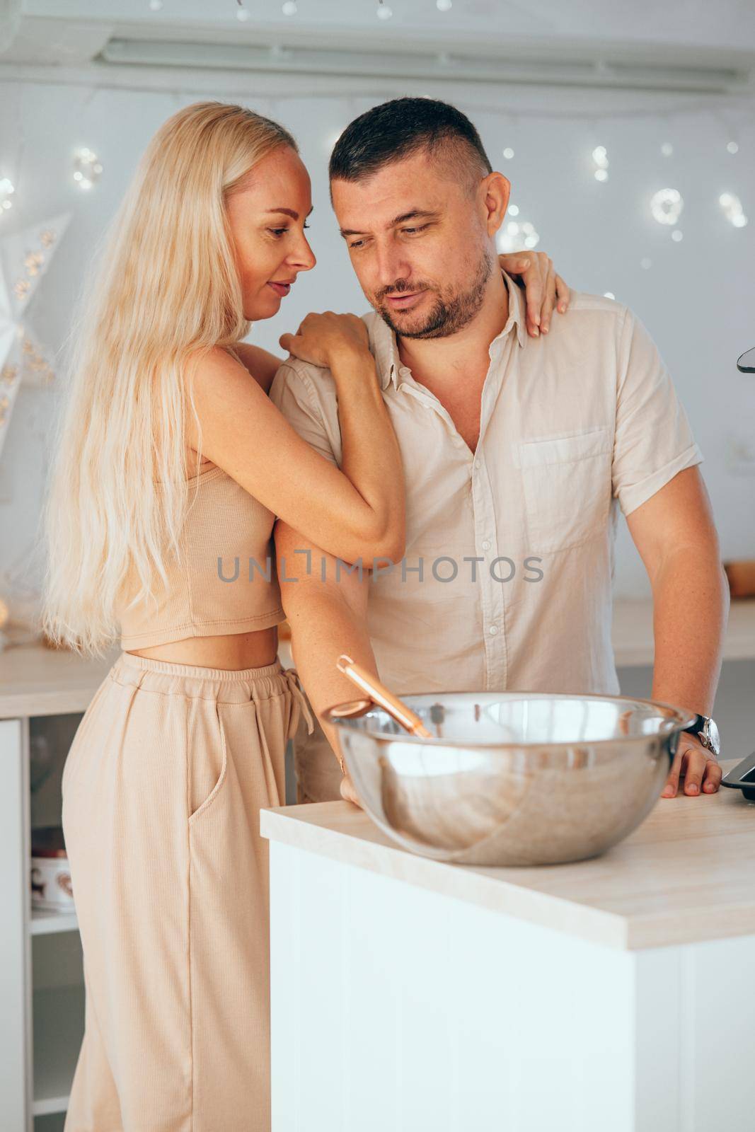 Young woman hugging her husband in kitchen while the preparation dough for Christmas cookies. Happy young couple husband and wife together, having fun making cookies at home in the kitchen.