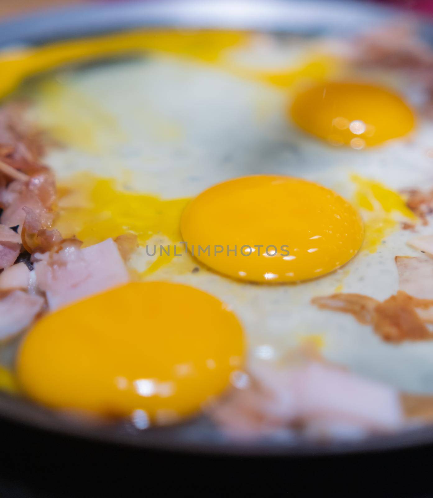 Close-up of chopped turkey ham and three raw egg yolks on a round griddle. Cooking thin turkey breast meat and scrambled eggs on frying pan. Healthy meal preparation
