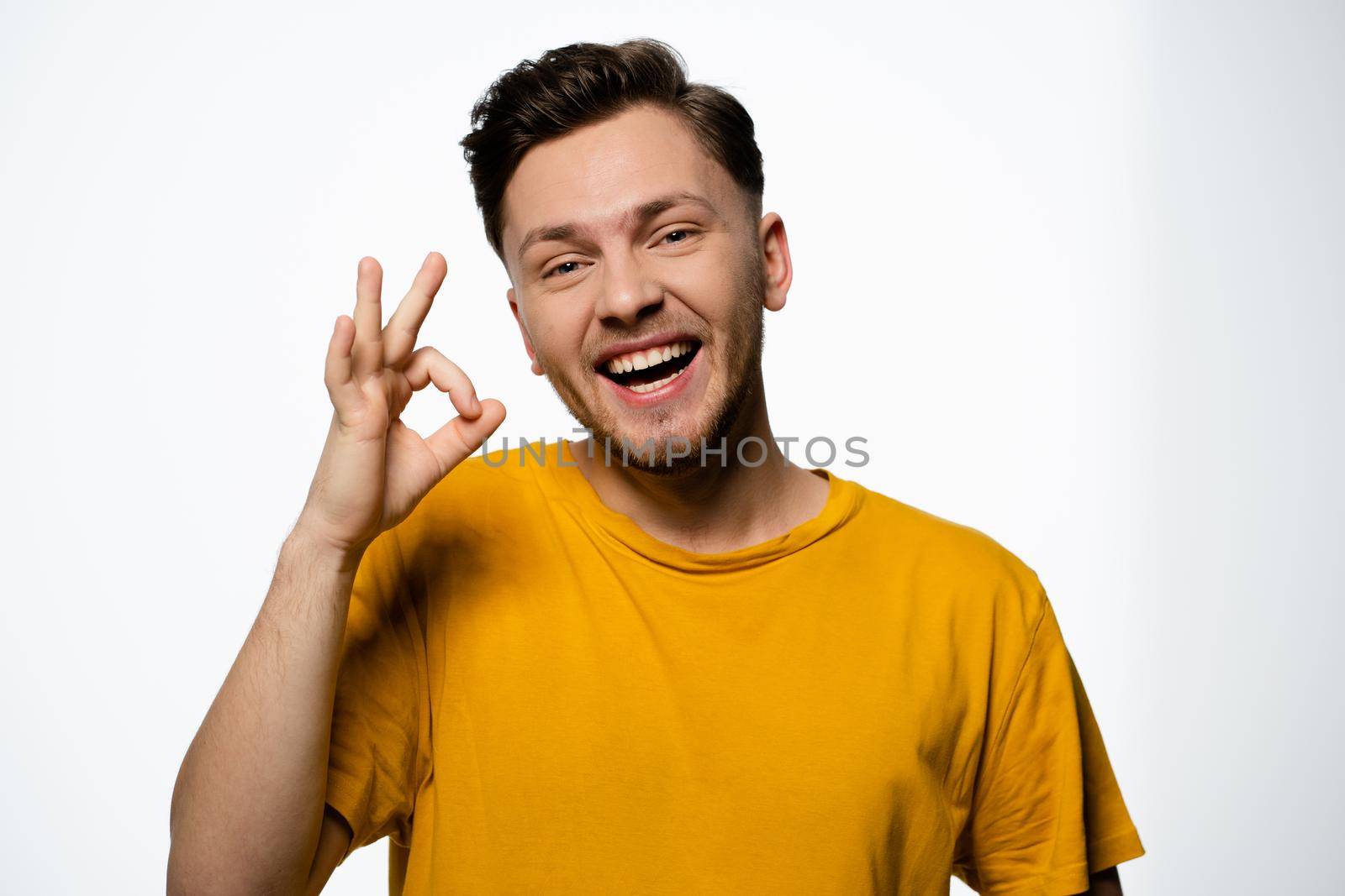 Cheerful Guy in a Yellow T-shirt Shows a Gesture of Okey on a White Background in the Studio. Positive Gesture, Ok Gesture. Copy Space. Close-up. High quality photo