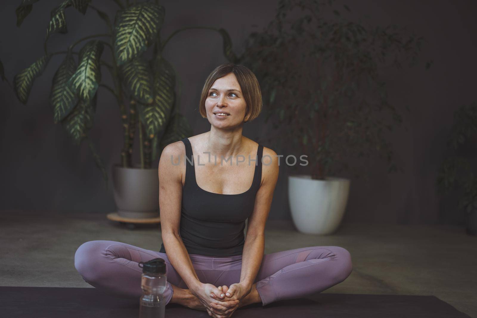 Happy young woman after a home yoga workout sits on a mat with a water bottle. Butterfly Pose. Concept of a healthy lifestyle, sports, care, longevity. High quality photo