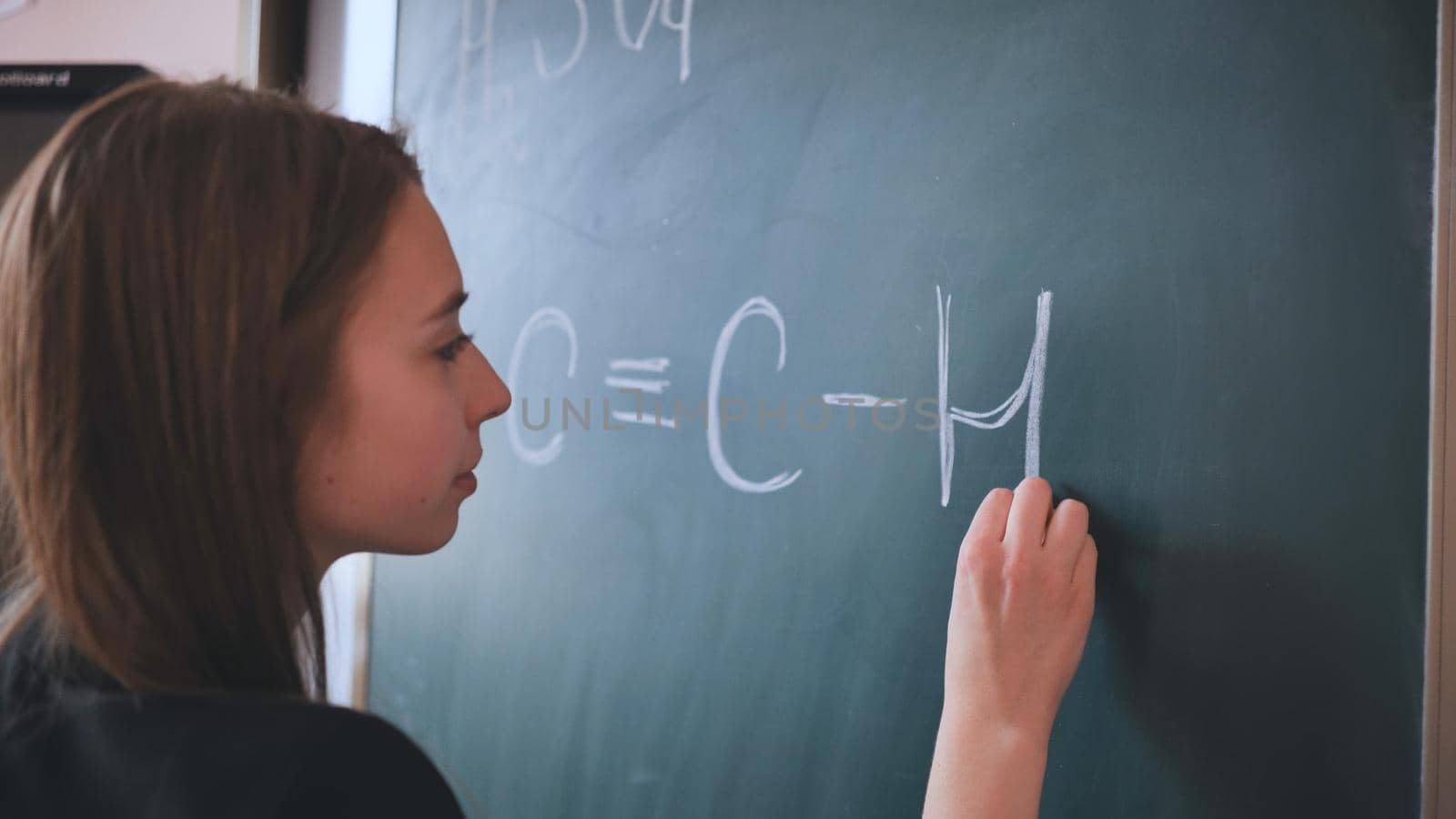 The girl is writing a chemical formula on the blackboard in the classroom