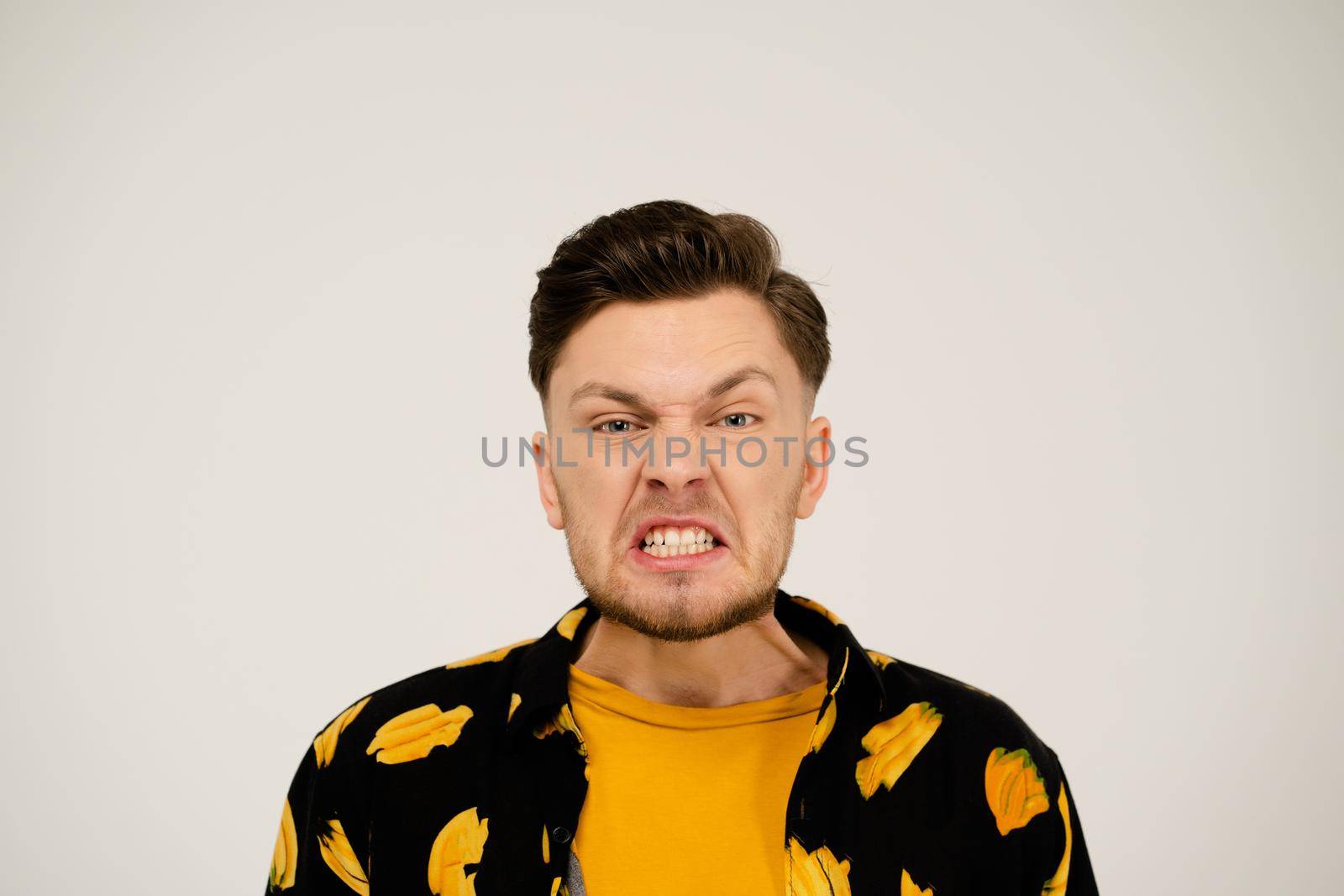 Negative Emotion to the Camera. Man in a Yellow T-shirt and a Funny Shirt on a White Background in the Studio. Angry Guy. Copy Space. Close-up. High quality photo