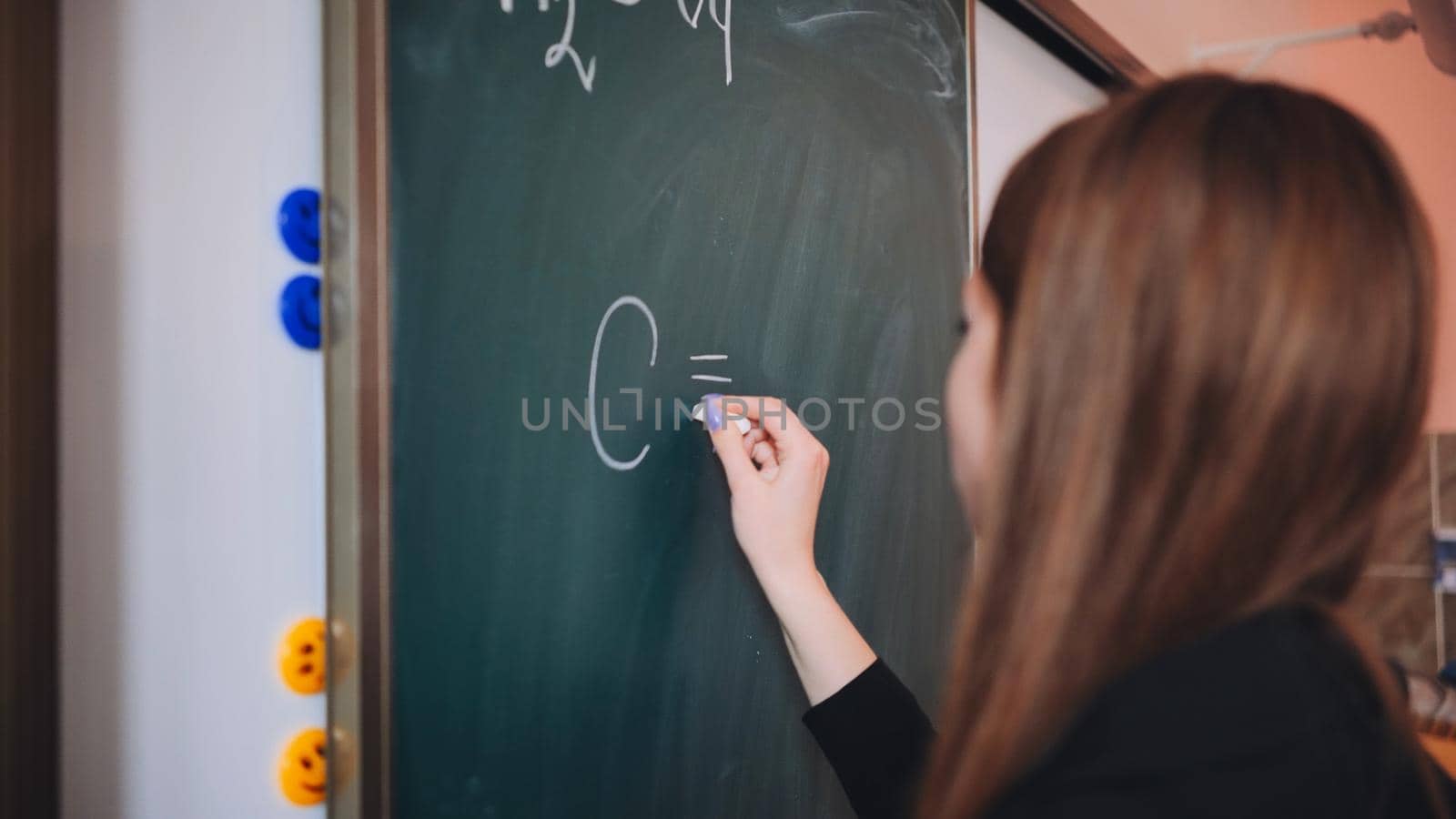 The girl is writing a chemical formula on the blackboard in the classroom. by DovidPro