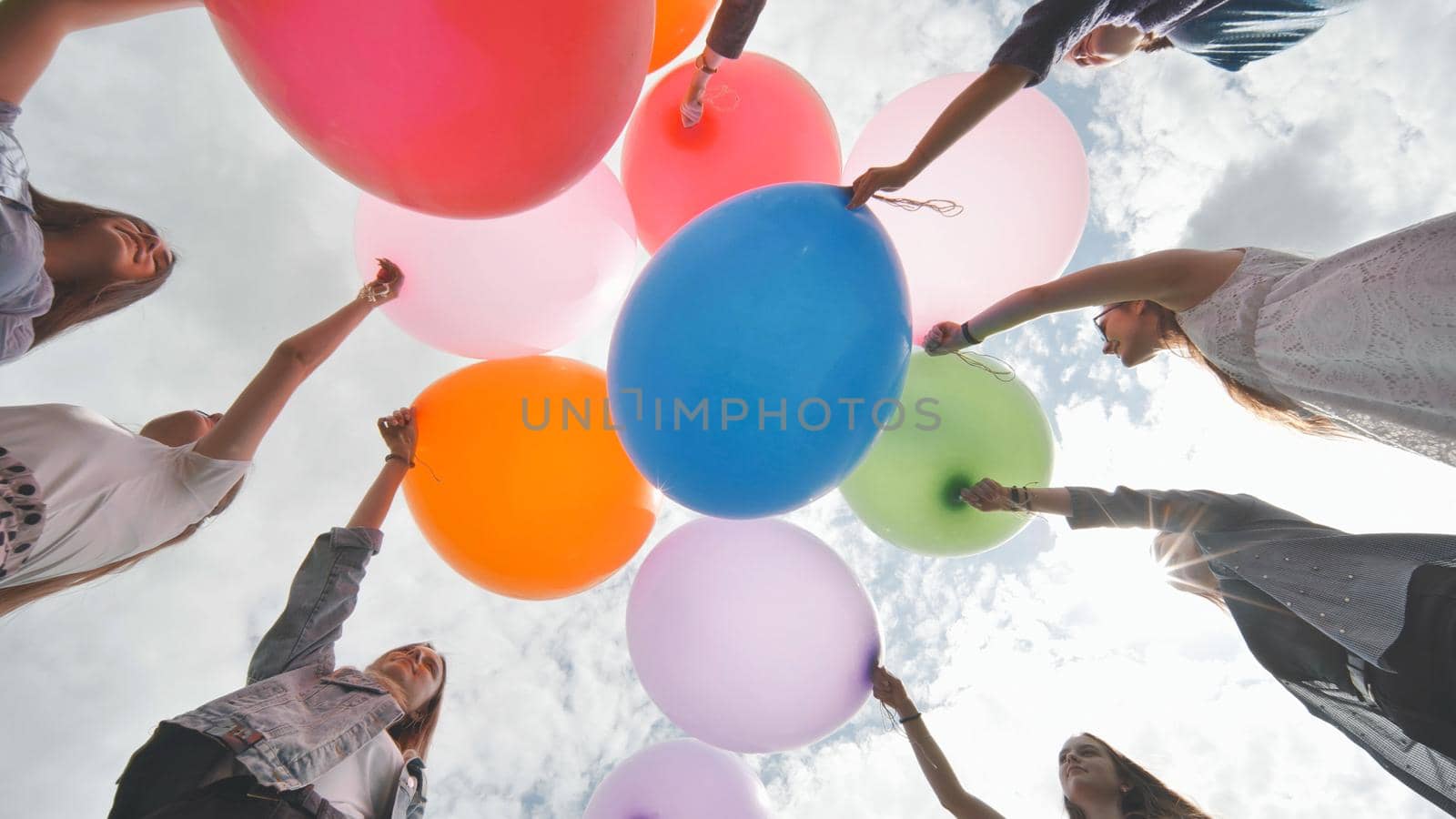 Cheerful girlfriends connect large colorful balls in a circle. by DovidPro