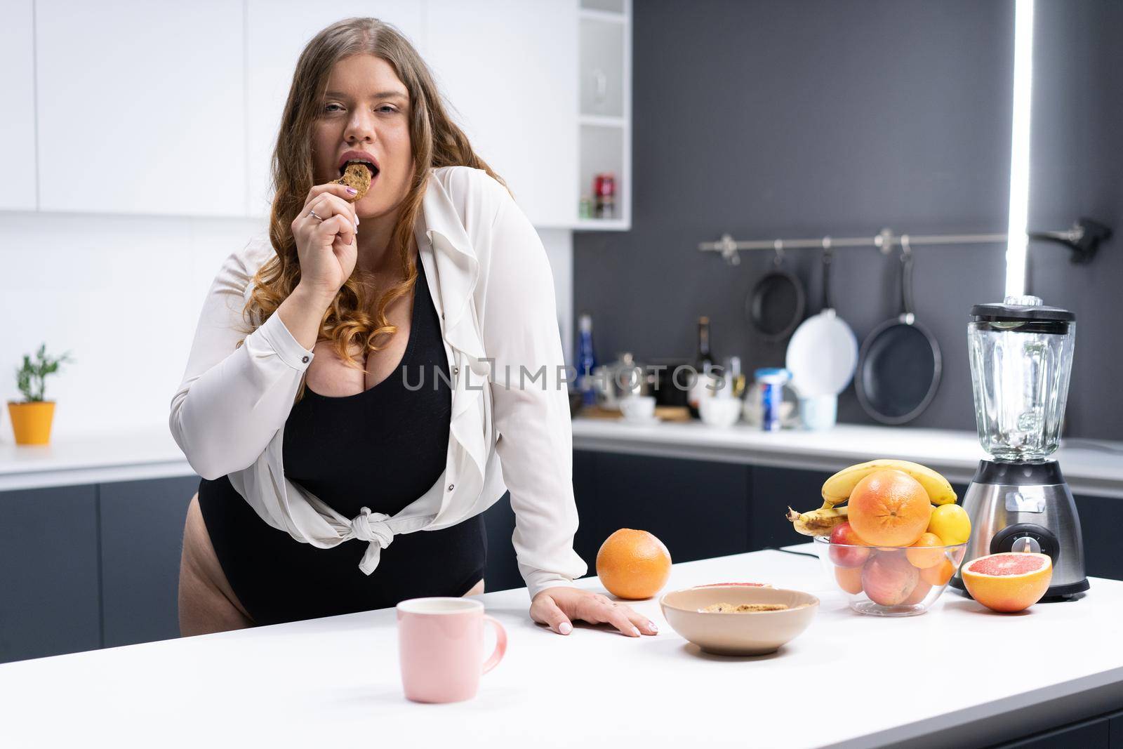 Sexy Woman Plus Size in Black Bodysuit and White Shirt has a Snack in the Kitchen. Healthy Food, Breakfast, Fruits, Citrus Fruits. Body Positive. Close-up. High quality photo
