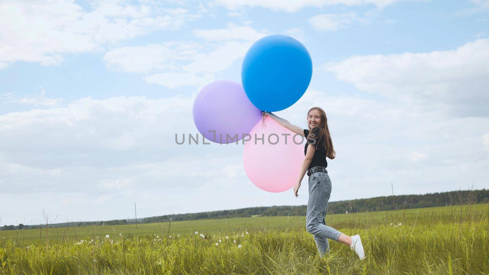 Happy girl with big multicolored balloons posing on the field. by DovidPro