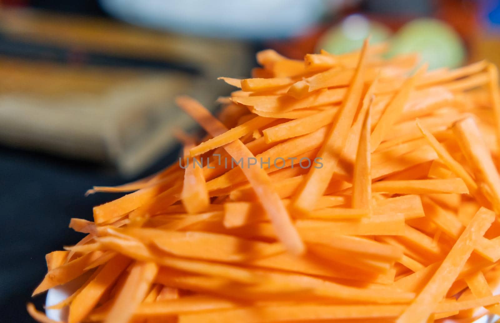 Close-up of small pile of thin carrot slices on white plate with blurry background. Tasty and fresh shredded carrot above porcelain plate. Healthy food preparation