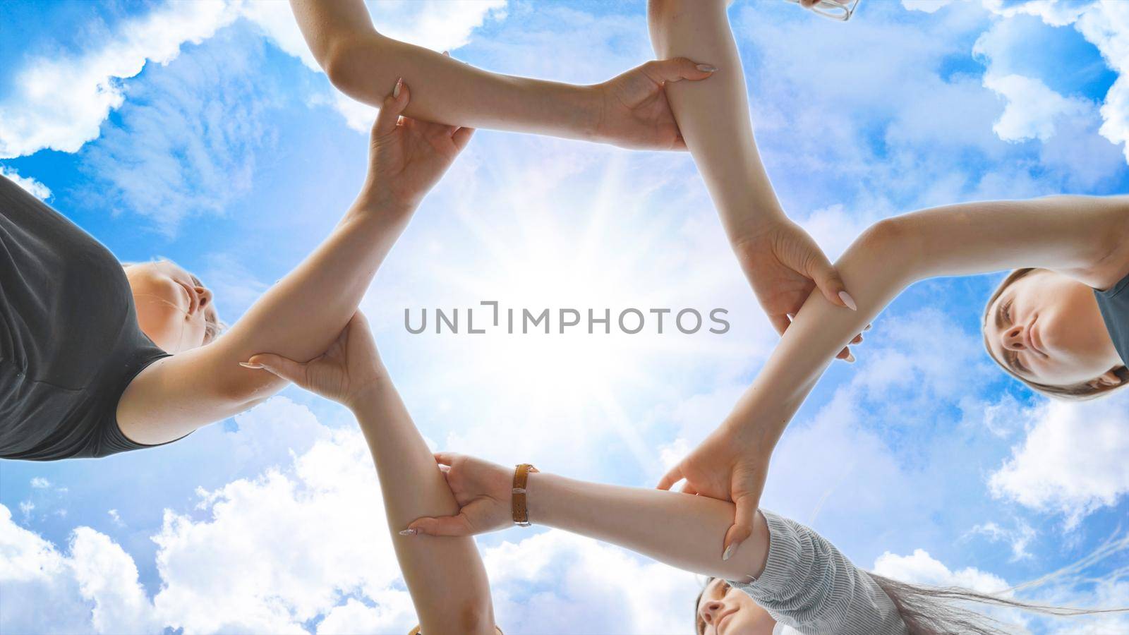 Friends join their hands by the wrist and make a circle against the backdrop of a fabulous sky. Strong friendship concept