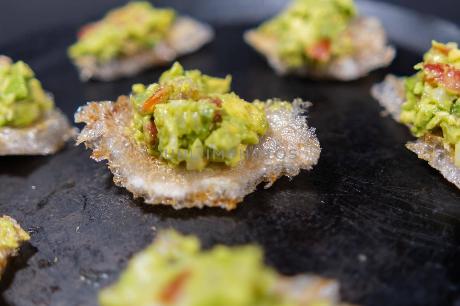 Close-up of delicious pork rinds with guacamole on traditional comal. Tasty avocado sauce on fried pork snacks above round griddle. Authentic Mexican food